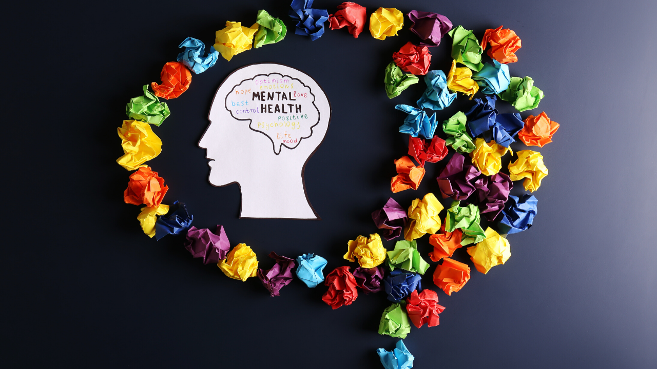 Various colored pieces of paper are crumpled up in the shape of a brain, and in the middle is a paper cut out of a person's head, with words that symbolize psychological capital and emotional intelligence.