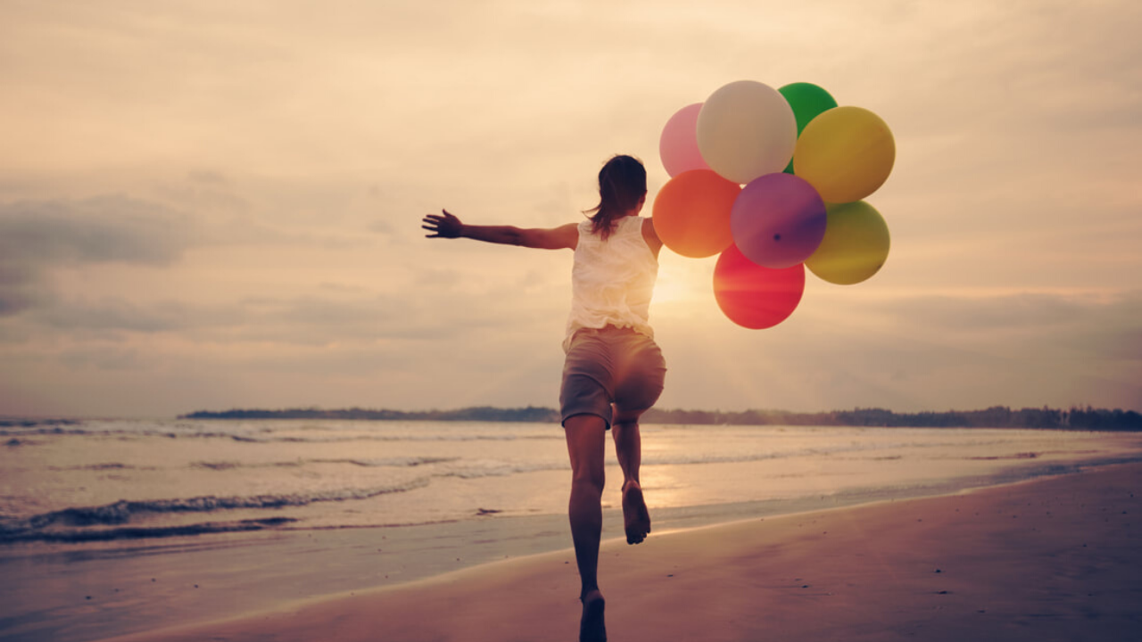 A woman runs on a beach with colorful balloons. She's clearly having fun!
