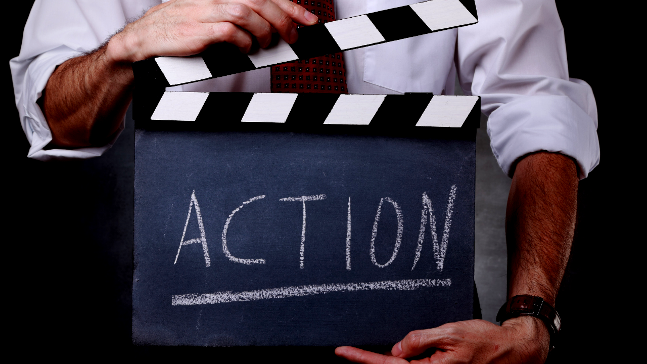 A man holds a movie set action sign that reads 