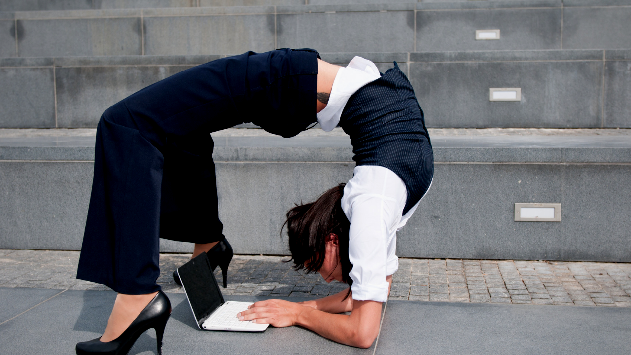 A business woman is bends over backwards while working on her laptop.