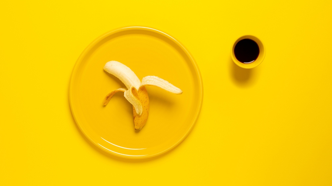 A banana, peeling on a yellow plate with a cup of coffee nearby.